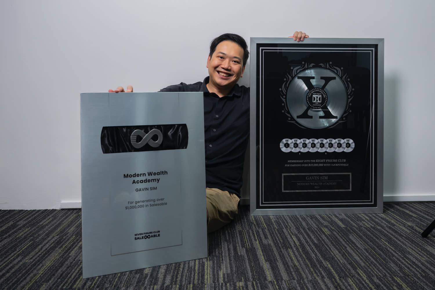 Gavin Sim holding his sales achievement awards, including an Eight Figure Club award